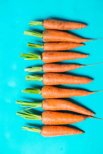 Several fresh carrots lie in a row on a blue background. — Stock Photo, Image