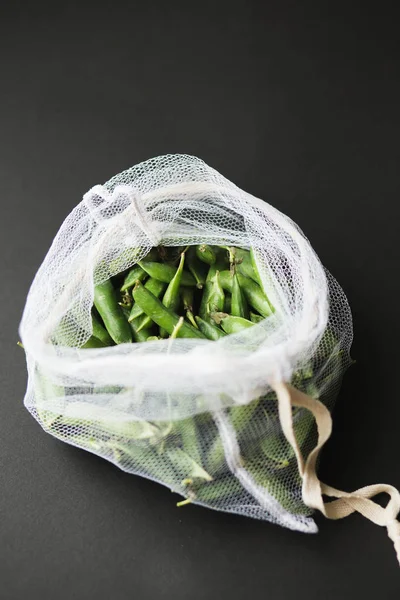 Reusable eco-friendly bag full of fresh seasonal pea pods on black background