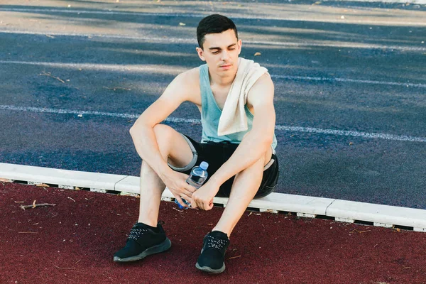 Dışarıda koşu yaptıktan sonra bir şişe suyla yerde oturan genç adam