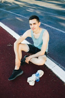 Dışarıda koşu yaptıktan sonra bir şişe suyla yerde oturan genç adam