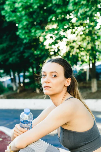 Bella donna seduta a terra con una bottiglia d'acqua dopo aver fatto jogging all'aperto — Foto Stock