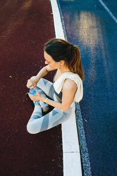Pretty kvinna sitter på marken med en flaska vatten efter jogging utomhus — Stockfoto