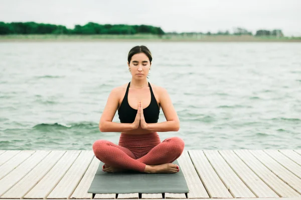 Ázsiai fiatal csinos lány meditál a szabadban, a mólón a tó. — Stock Fotó