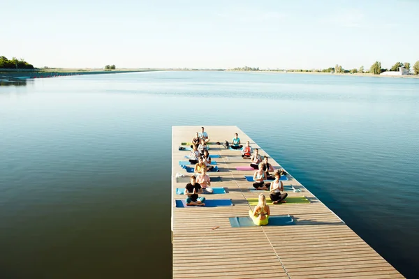 Eine große Gruppe von Yoga-Teilnehmern auf einem Ponton in der Nähe des Sees. — Stockfoto