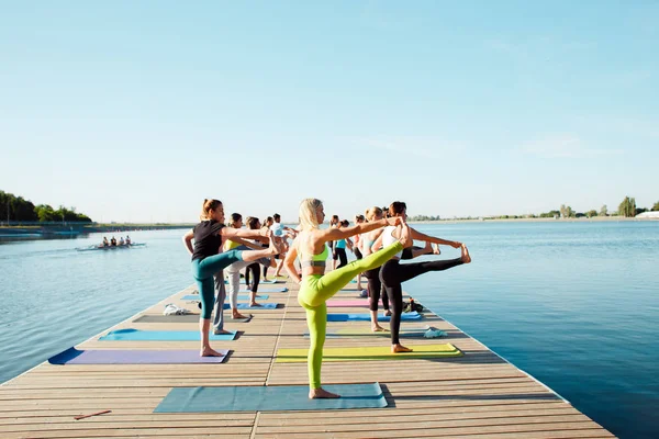 Eine große Gruppe von Yoga-Teilnehmern auf einem Ponton in der Nähe des Sees. — Stockfoto