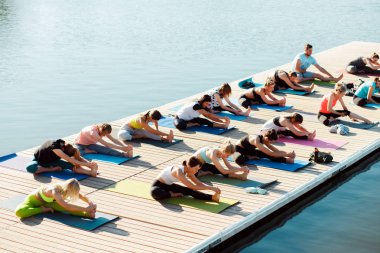 Gölün yakınındaki bir pontonda yoga derslerine katılan büyük bir grup insan..