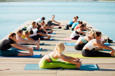 Gölün yakınındaki bir pontonda yoga derslerine katılan büyük bir grup insan..
