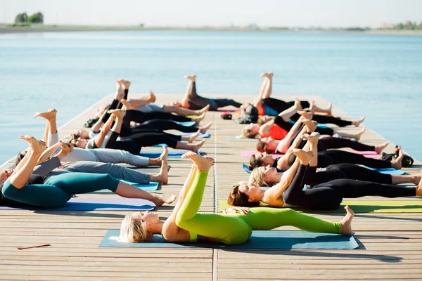 A big group of people attending yoga classes on a pontoon near the lake. — Stock Photo, Image