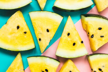 mavi-pembe arka plan üzerinde olgun sarı karpuz üçgen dilimleri kesti