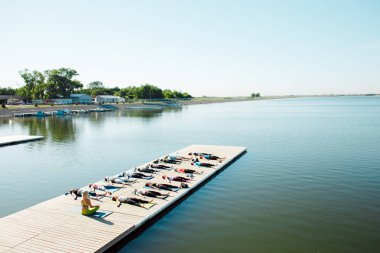 Gölün yakınındaki bir pontonda yoga derslerine katılan büyük bir grup insan..