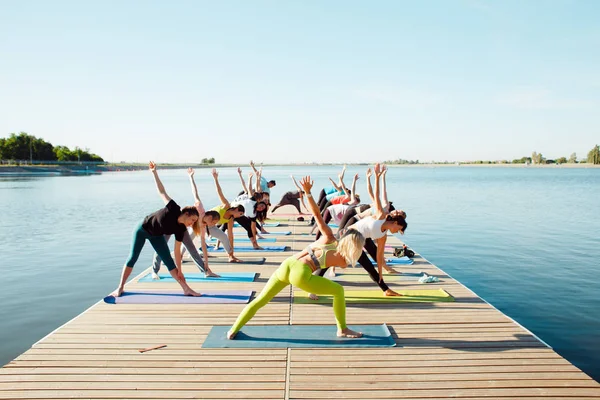Gölün yakınındaki bir pontonda yoga derslerine katılan büyük bir grup insan..