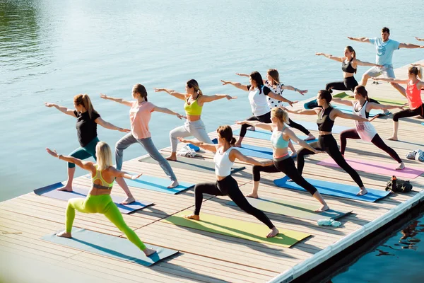 Gölün yakınındaki bir pontonda yoga derslerine katılan büyük bir grup insan..
