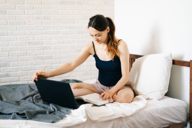 Laptop kullanan genç bir kadın, virüs karantinadayken internet üzerinden müşterisiyle iletişim kuruyor. Rahat ofis yeri, uzaktan çalışma, e-öğrenme konsepti.