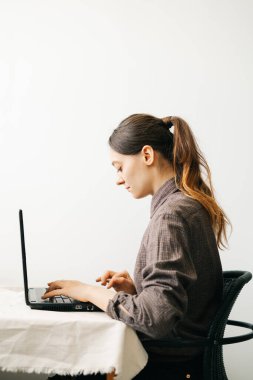 Bilgisayarında virüs karantinası sırasında evden çalışan genç bir Avrupalı kadın var. Kız minimalist bir iç mekanda beyaz bir masada oturuyor. Rahat bir iş yeri, uzaktan çalışma konsepti.,