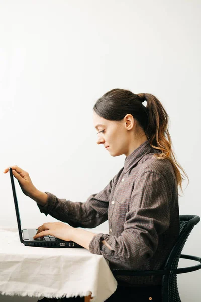 一位年轻的欧洲妇女 在病毒检疫期间在家工作 在她的笔记本电脑上 这个女孩正坐在一张白色的桌子旁 在一间简约的屋子里 一个舒适的工作场所 一个遥远工作的概念 — 图库照片