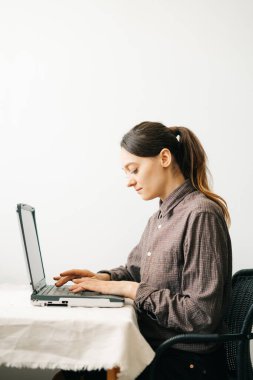 Bilgisayarında virüs karantinası sırasında evden çalışan genç bir Avrupalı kadın var. Kız minimalist bir iç mekanda beyaz bir masada oturuyor. Rahat bir iş yeri, uzaktan çalışma konsepti.,