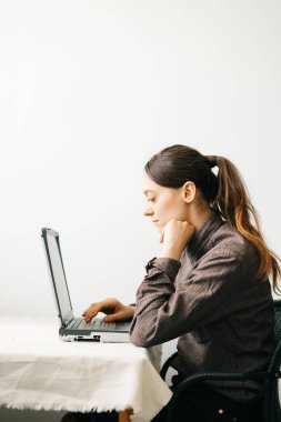 Bilgisayarında virüs karantinası sırasında evden çalışan genç bir Avrupalı kadın var. Kız minimalist bir iç mekanda beyaz bir masada oturuyor. Rahat bir iş yeri, uzaktan çalışma konsepti.,