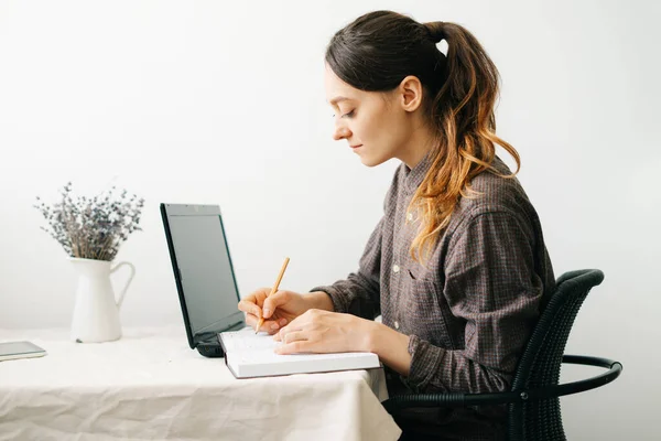 a young woman who works from home while the virus is quarantined on her laptop, studies information on the Internet and writes notes in a diary.A cosy working place,the concept of remote work