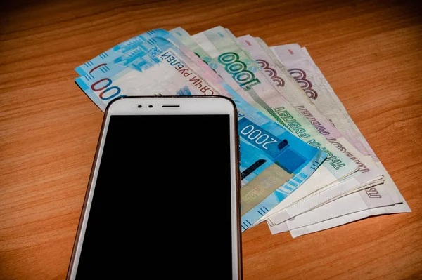 Ruské bankovky a mobilní telefon na dřevěný stůl. — Stock fotografie