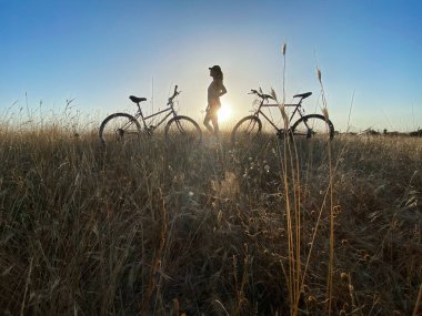 Gün batımında bisikletli genç bir kadının silueti.