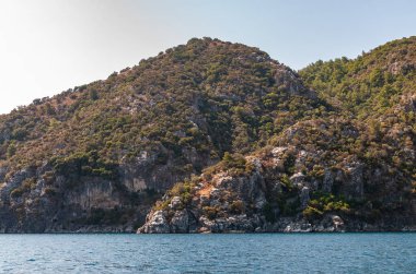 Türkiye 'nin Ege sahili manzarası. Dağları, yemyeşil bitkileri, kayalık kıyıları ve turkuaz suyu olan resimli bir kıyı manzarası..
