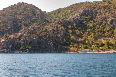 Türkiye 'nin Ege sahili manzarası. Dağları, yemyeşil bitkileri, kayalık kıyıları ve turkuaz suyu olan resimli bir kıyı manzarası..