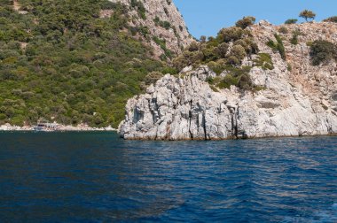Türkiye 'nin Ege sahili manzarası. Dağları, yemyeşil bitkileri, kayalık kıyıları ve turkuaz suyu olan resimli bir kıyı manzarası..
