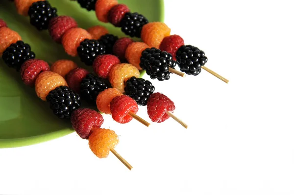 Шампуры малиновых ягод разных цветов на зеленой тарелке на белом фоне — стоковое фото