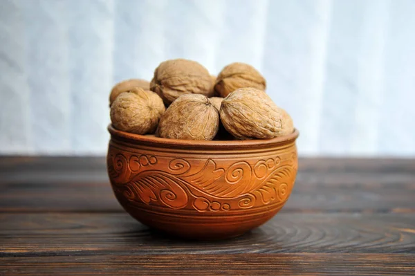 Ongepelde walnoten in aardewerk op een houten tafel — Stockfoto