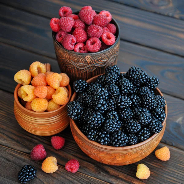 Bayas de color rojo, amarillo y negro frambuesas o moras en loza sobre una mesa de madera — Foto de Stock