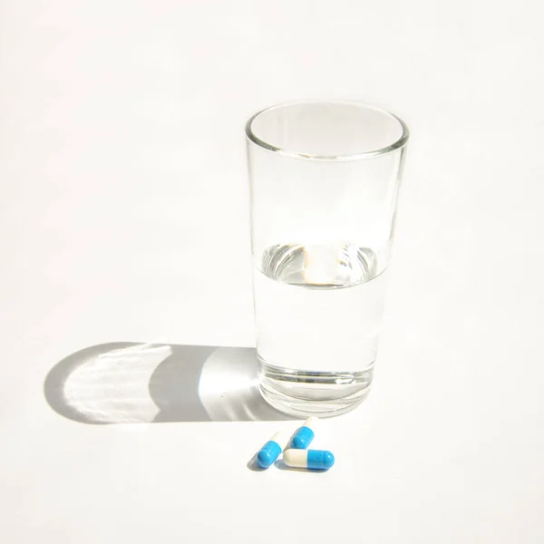 Glass of water with medical capsules on a white — Stock Photo, Image