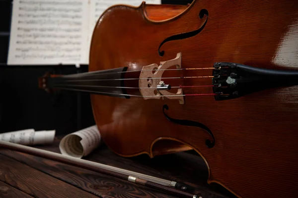 大提琴躺在木制表面上 上有弓和乐谱 案文的位置 — 图库照片