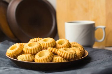 Siyah peçete üzerinde sarı kurabiye ve beyaz kupa ile plaka