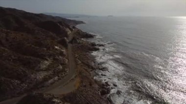 Dalgaların kayalara çarptığı deniz ve deniz kenarındaki yol.