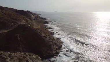 Dalgaların kayalara çarptığı deniz ve deniz kenarındaki yol.