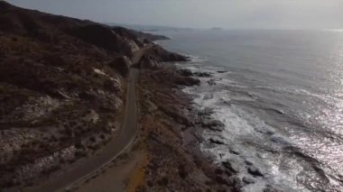 Dalgaların kayalara çarptığı deniz ve deniz kenarındaki yol.