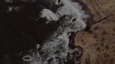 Dalgaların kayalara çarptığı deniz ve deniz kenarındaki yol.