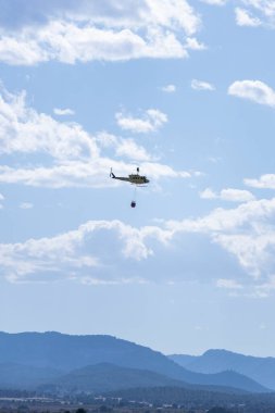 Helikopterler gökyüzünden suyla dağda büyük bir yangın çıkarıyorlar.