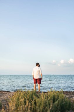 Sonbahar günbatımında denize bakan maskeli bir adam.