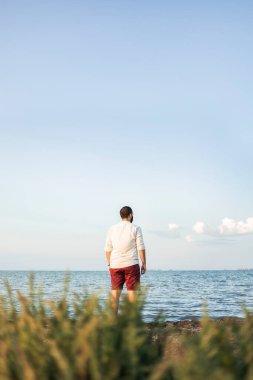 Sonbahar günbatımında denize bakan maskeli bir adam.