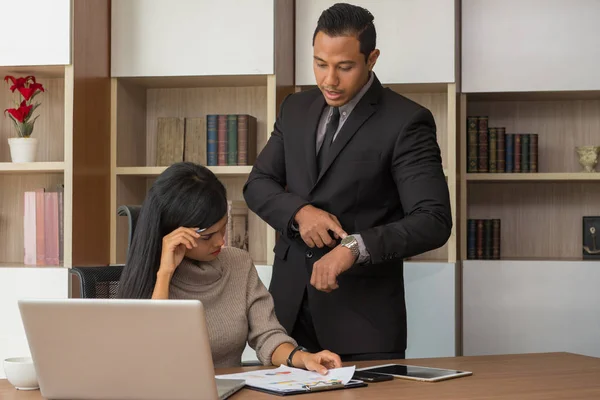 Upset woman being scolded by boss for working at office and Boss point to clock showing time for deadline job.