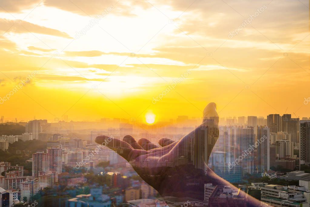 Double exposure of Hand holding sunset on cityscape background.