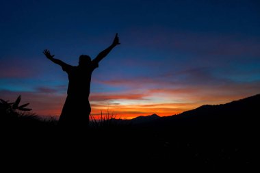 Gezgin ile eller yukarı günbatımında dağ silueti.