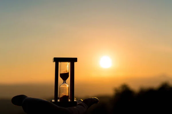 Ruka držící přesýpací hodiny s východem slunce ráno, pojem o čase — Stock fotografie