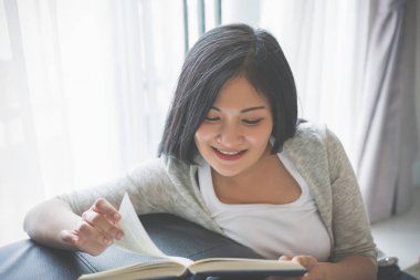 Evde yatakta kitap okuyan genç bir kadın.