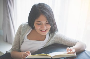 Evde yatakta kitap okuyan genç bir kadın.