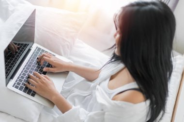 Dizüstü bilgisayarda çalışan genç bir kadın evde yatağında oturuyor.