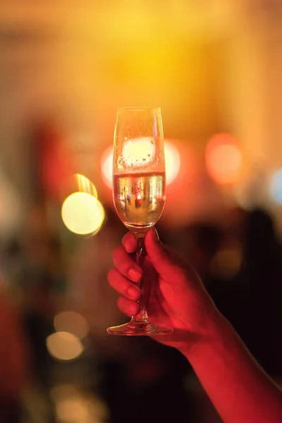 man hand is holding a glass of white wine in night party