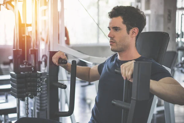 Handsome man lowering weight of fitness machine and working out — Stock Photo, Image