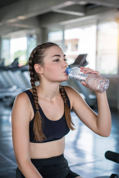 Beautiful young woman drinks water in gym. Sports nutrition conc